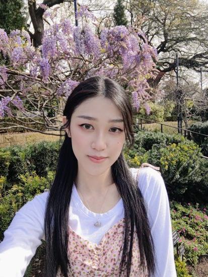 A woman taking a self-portrait with garden scenery behind her.