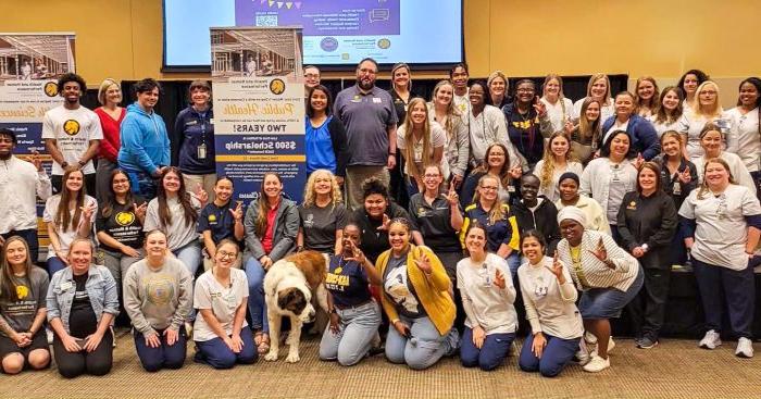 A large group of college students, faculty and staff posing while displaying the "Lucky Lion" hand symbol.